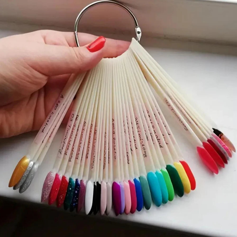 A hand holds a set of nail art practice false tips, featuring various colors and designs, hanging from a metal loop.