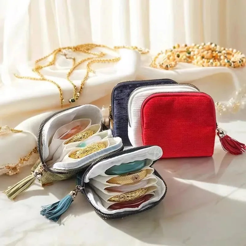 A red velvet jewelry storage bag with a black zipper and tassel is shown open, revealing various gold and silver jewelry piec
