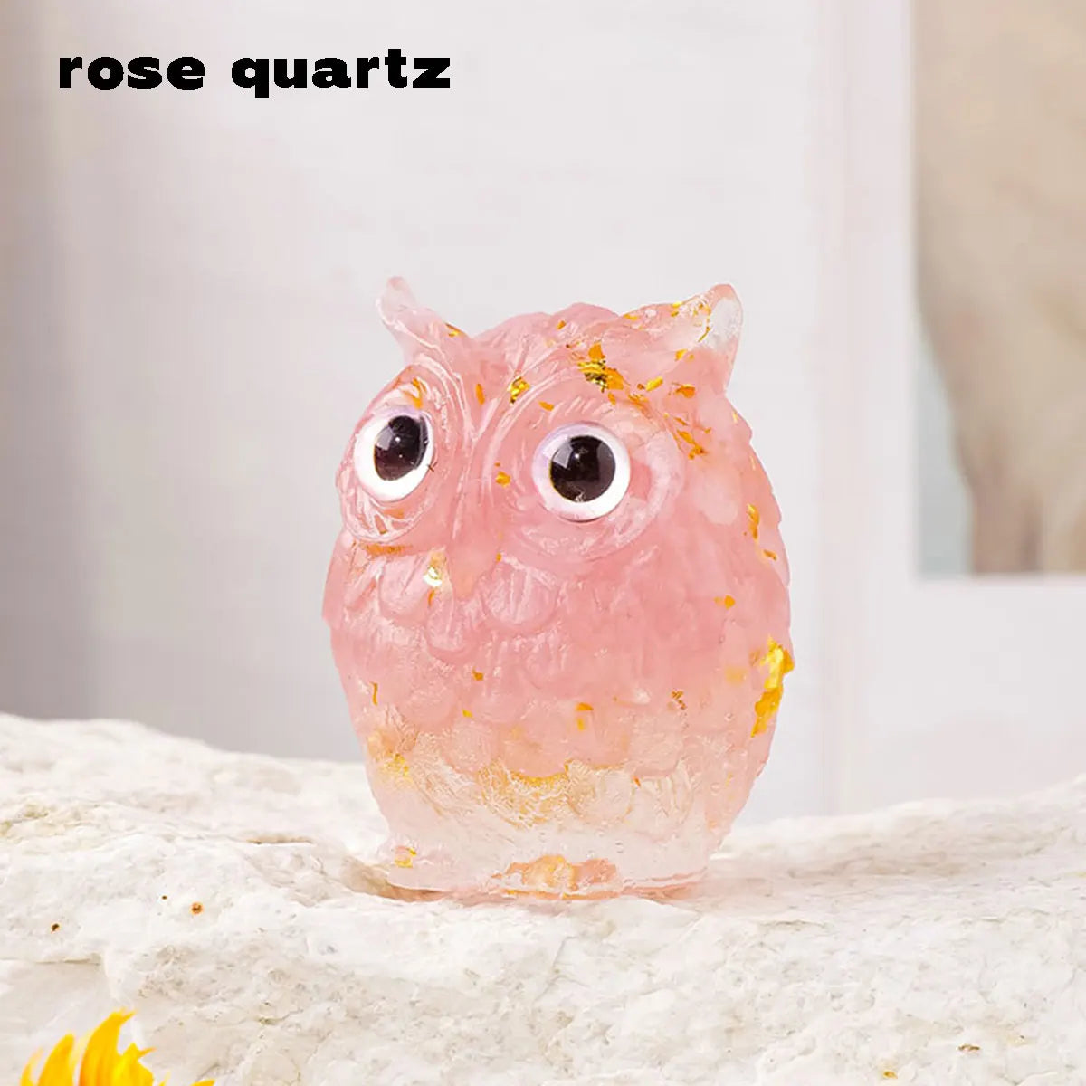 Adorno de cuarzo rosa en forma de búho con destellos dorados, sobre una superficie blanca.