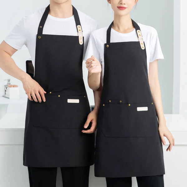 A woman and a man wearing black waterproof canvas chef aprons over white shirts.