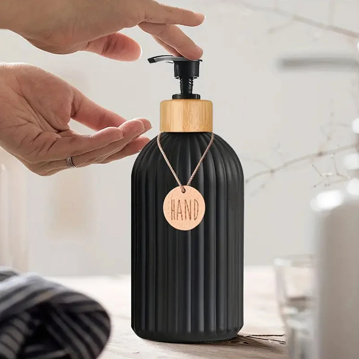 Eine Hand dispense Flüssigkeit aus einer mattschwarzen wiederbefüllbaren Seifenspenderflasche mit Holzverschluss und goldener
