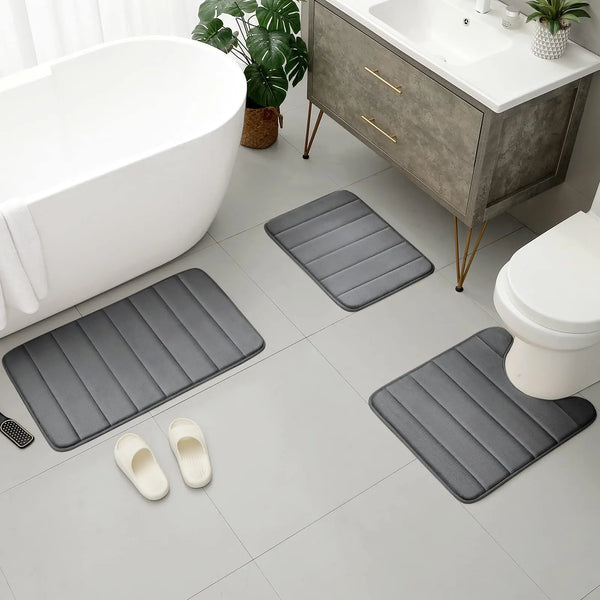 A set of three gray memory foam bathroom mats placed on a light tile floor near a vanity and toilet.