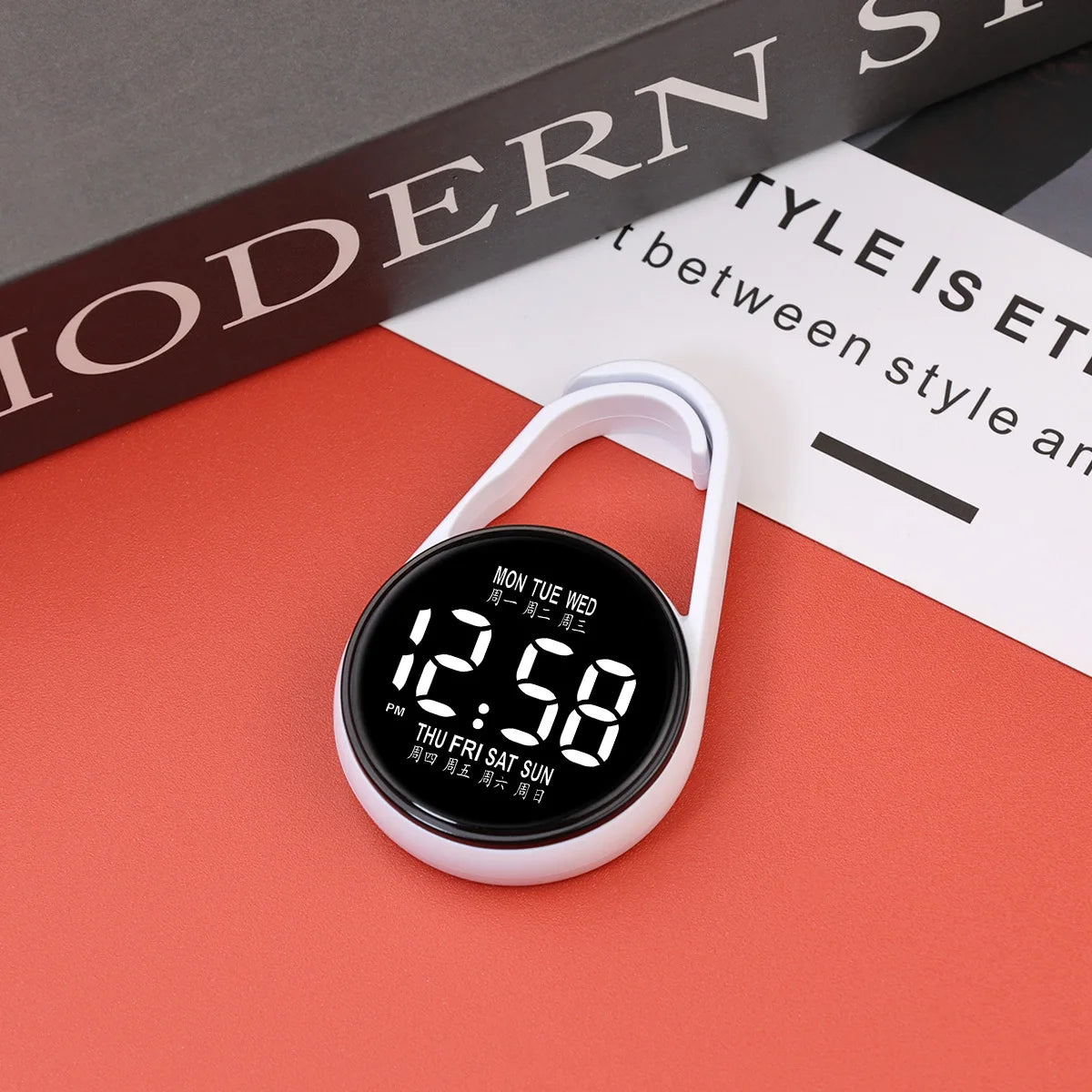 A white digital LED hanging pocket watch displaying 12:58 on a red surface.