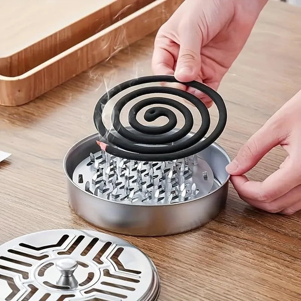 A hand is placing a coiled mosquito coil into a stainless steel tray holder on a wooden surface.