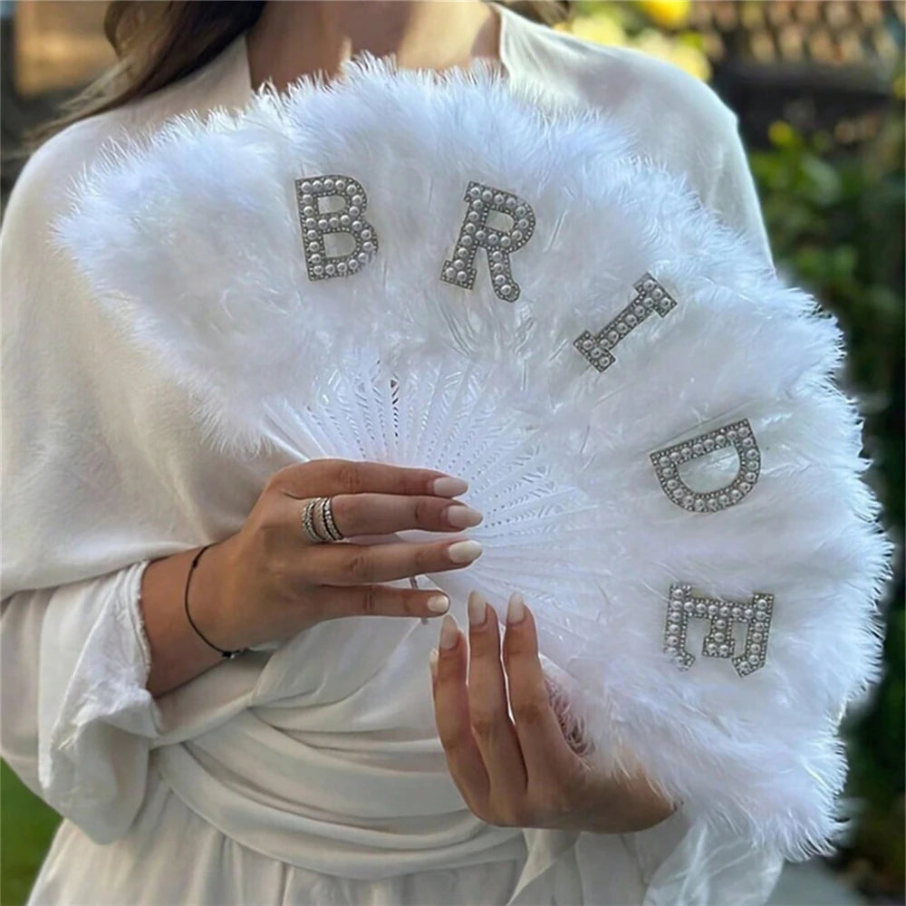 A woman holds a white feather hand fan decorated with silver letters B R I D E to bridal decor.
