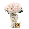 A golden and white ceramic flower vase holding a bouquet of light pink flowers.