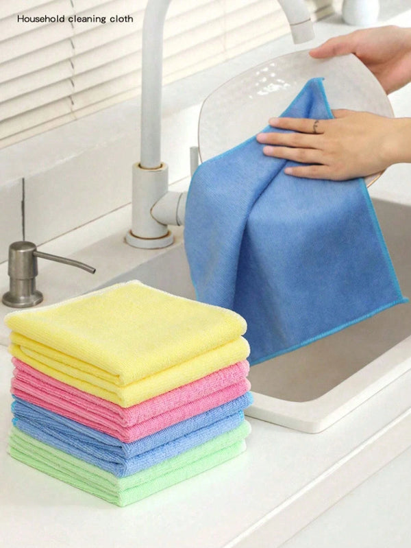 Eine Hand wischt einen blauen Mikrofasertuch über eine Küchenspüle, mit einem Stapel bunter Reinigungstücher in der Nähe.