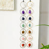 A string of seven crystal healing ornaments, featuring various colored stones like amethyst, sapphire, and jade, displayed ag