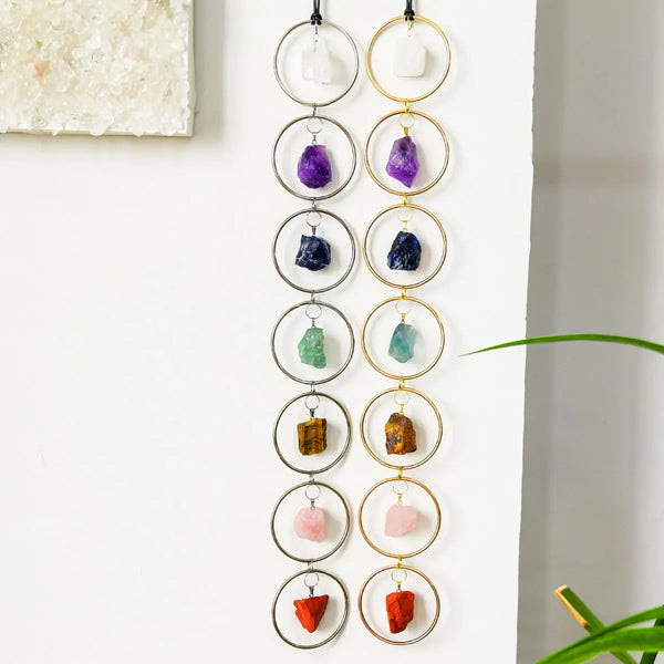 A string of seven crystal healing ornaments, featuring various colored stones like amethyst, sapphire, and jade, displayed ag