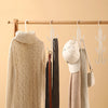 A beige knitted sweater and a white baseball cap are hanging on a wooden rack with wire hangers.