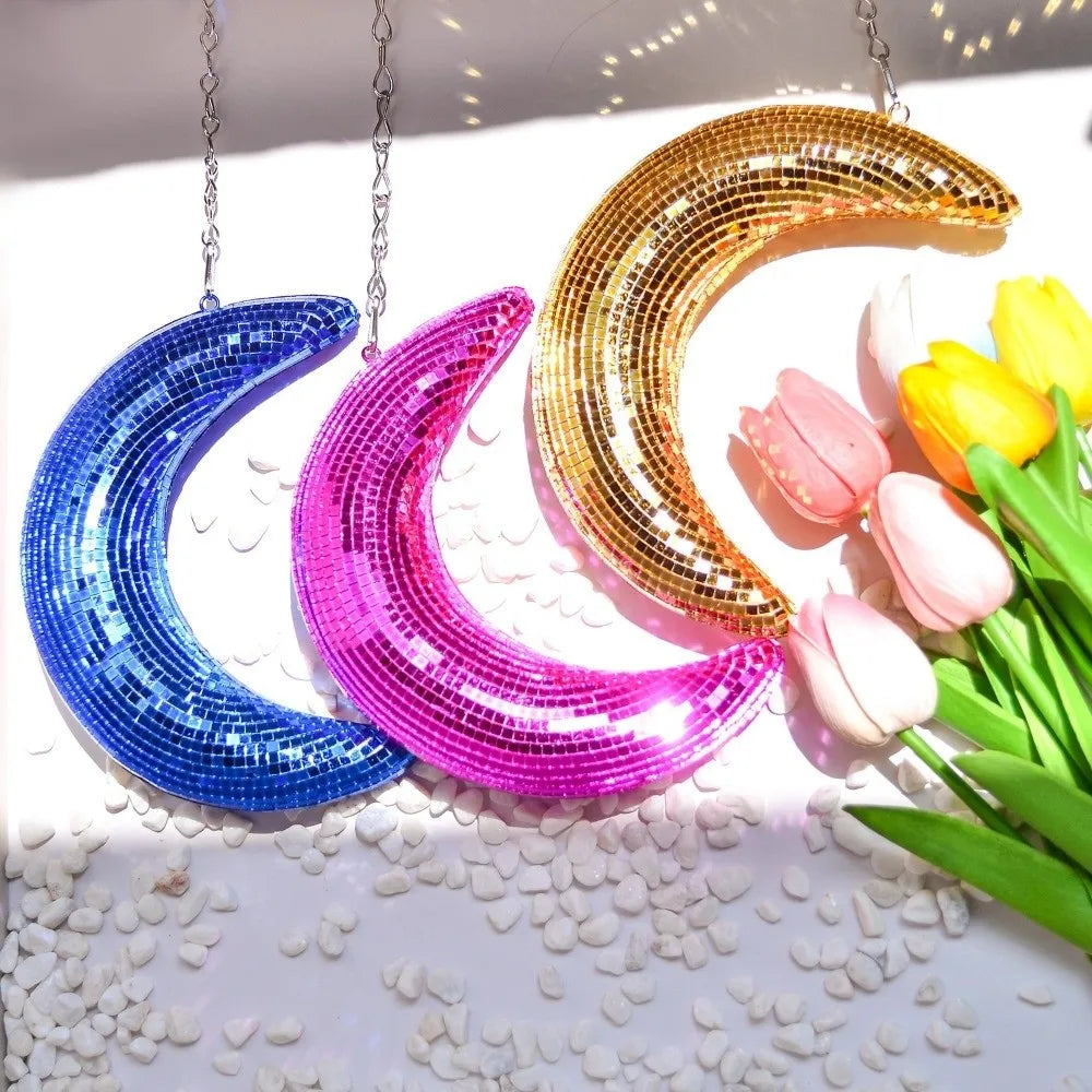 Three colorful, crescent moon pendants made of iridescent glass or acrylic are displayed on a white surface.