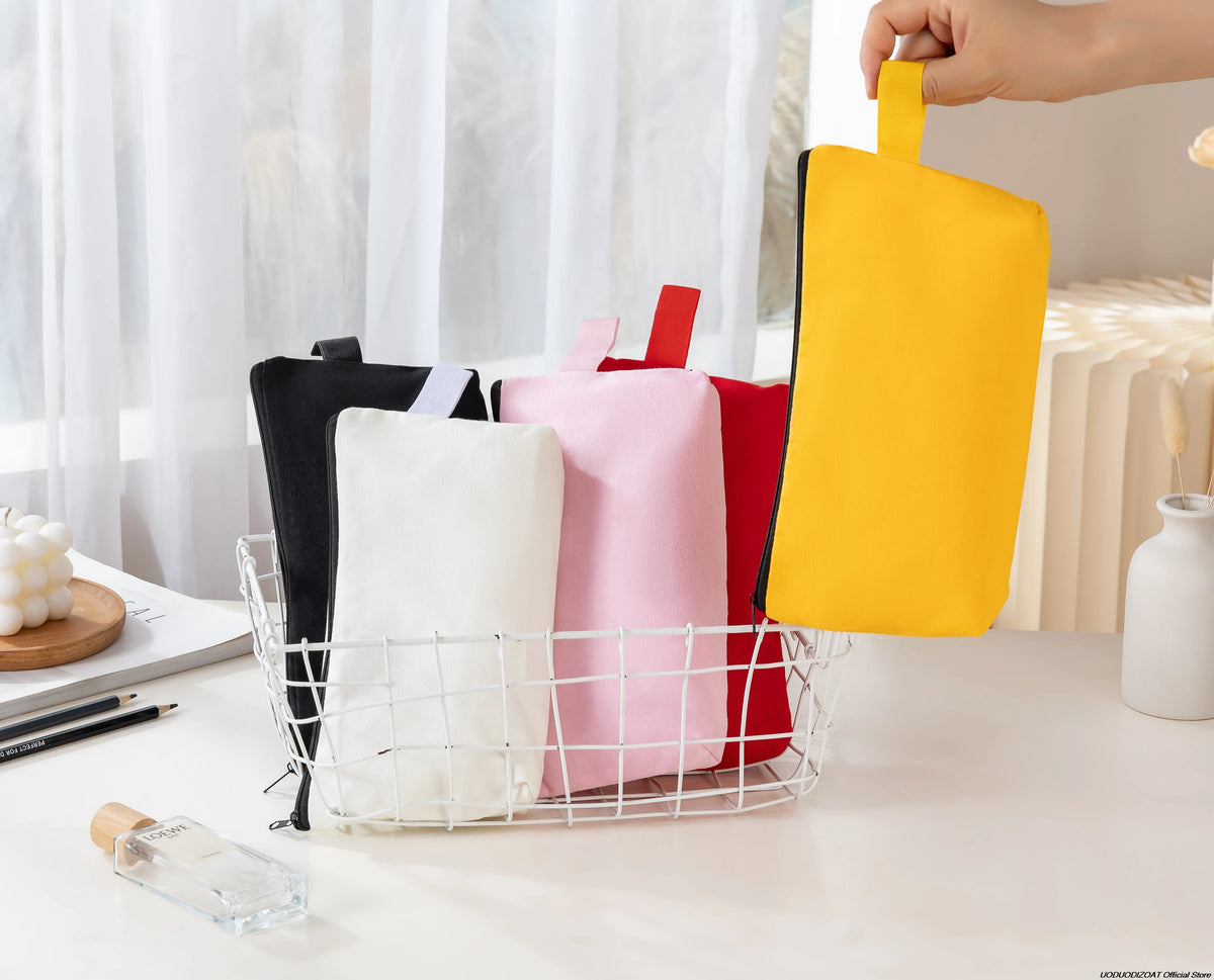 A hand is holding a bright yellow zipper bag among several pink and black bags stored in a white wire basket.