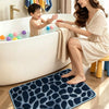A woman is sitting by a bathtub with a child, and a dark blue pebble embossed bath mat is placed on the floor.