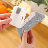 A hand holds a white cleaning brush with a gray grip and a soft, fuzzy cleaning pad for cleaning electronics.