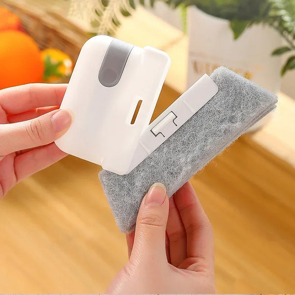A hand holds a white cleaning brush with a gray grip and a soft, fuzzy cleaning pad for cleaning electronics.