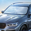 A silver car with a transparent sunshade installed on the windshield for protection.