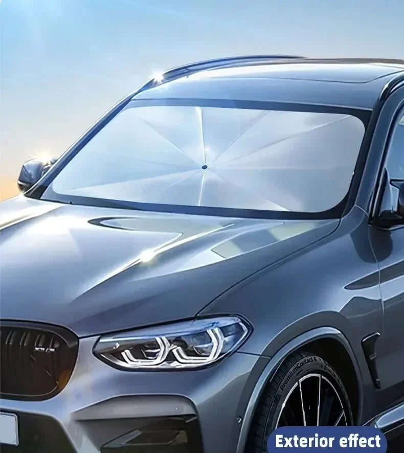 A silver car with a transparent sunshade installed on the windshield for protection.
