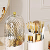 A clear spherical organizer with a gold lid holds various makeup brushes and tools for organization.