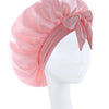 Pink silky satin sleep bonnet tied with a bow displayed on a white mannequin head.