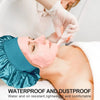 A person is applying a pink facial mask to a woman's face while wearing a teal satin sleeping bonnet.