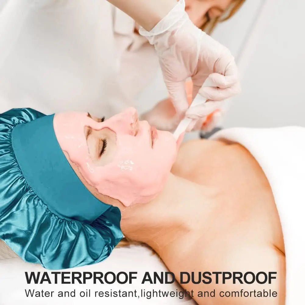 A person is applying a pink facial mask to a woman's face while wearing a teal satin sleeping bonnet.