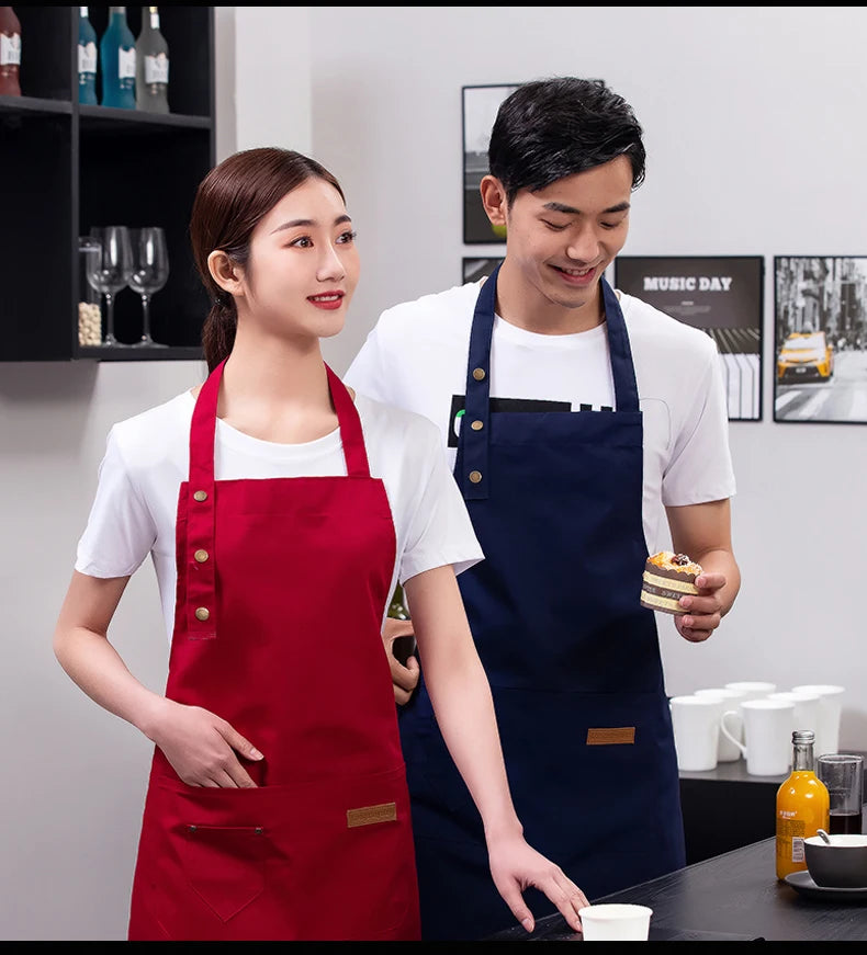 A woman in a red apron stands next to a man in a navy blue apron, both in a bright kitchen setting.