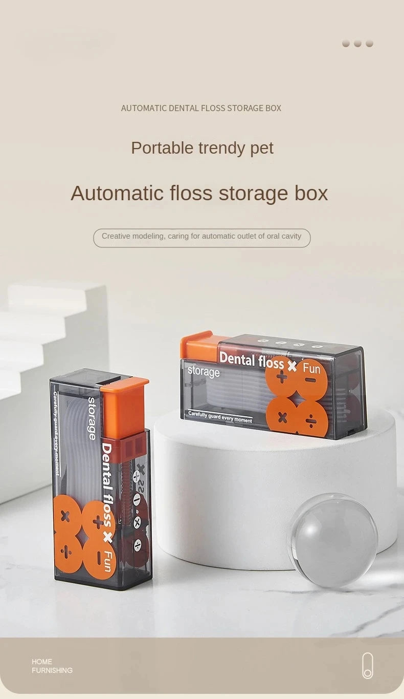 Caja automática para hilo dental en naranja y negro, junto a un recipiente de cerámica blanca.