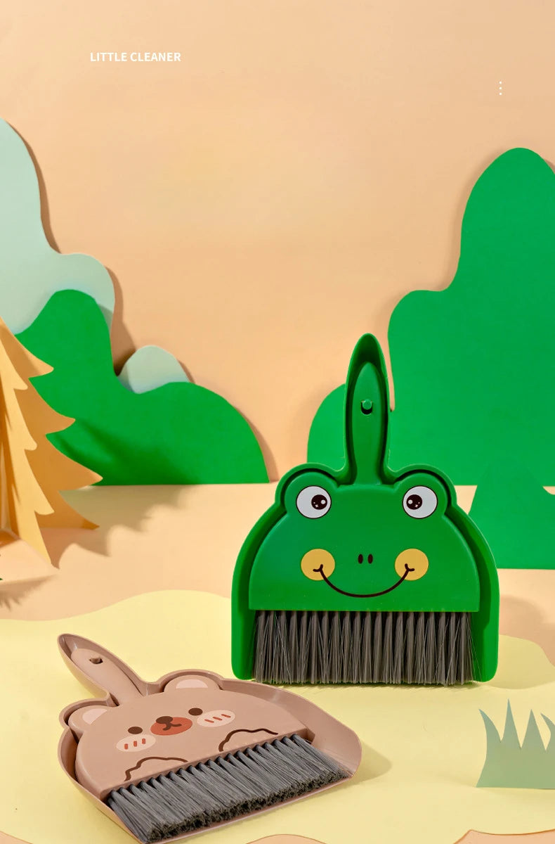 A green cartoon animal broom and dustpan set with a smiling face is shown on a light background.