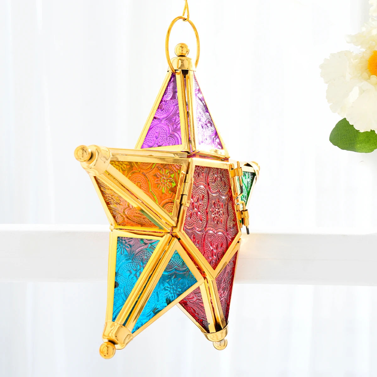 A forged iron star hanging candlestick with multicolored stained glass panels.