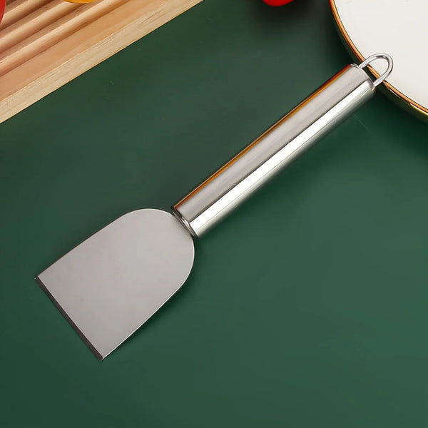 A stainless steel multi-purpose scraper with a handle and blade resting on a dark green surface.