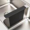 A black non-slip silicone kitchen sink protector mat with drainage is shown inside a stainless steel sink.