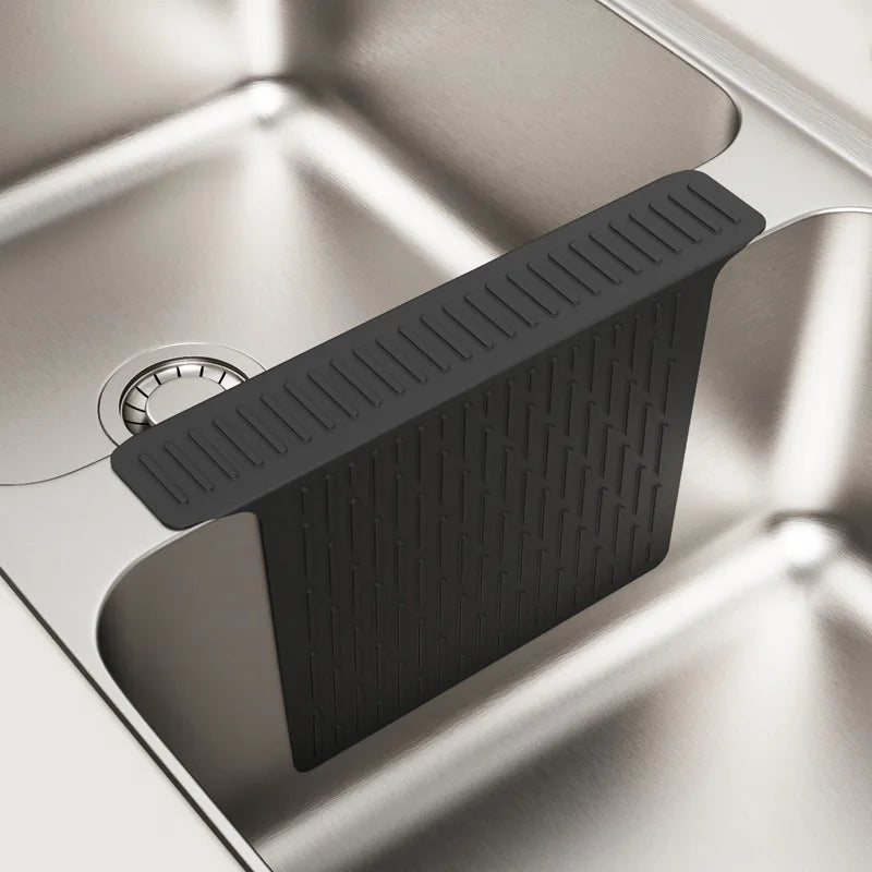 A black non-slip silicone kitchen sink protector mat with drainage is shown inside a stainless steel sink.