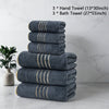 A stack of three dark gray hand towels and three bath towels with gold trim on a white marble surface.