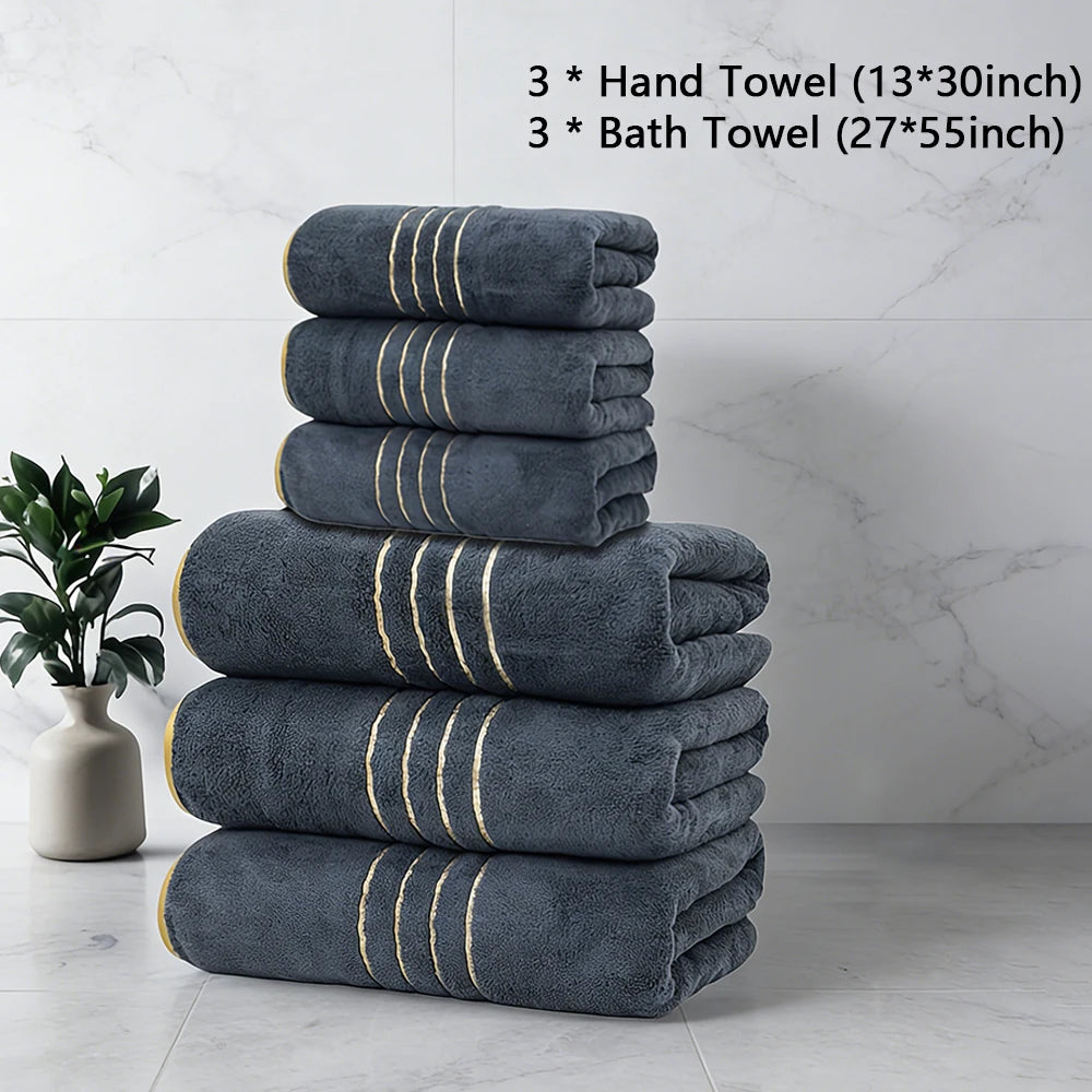 A stack of three dark gray hand towels and three bath towels with gold trim on a white marble surface.