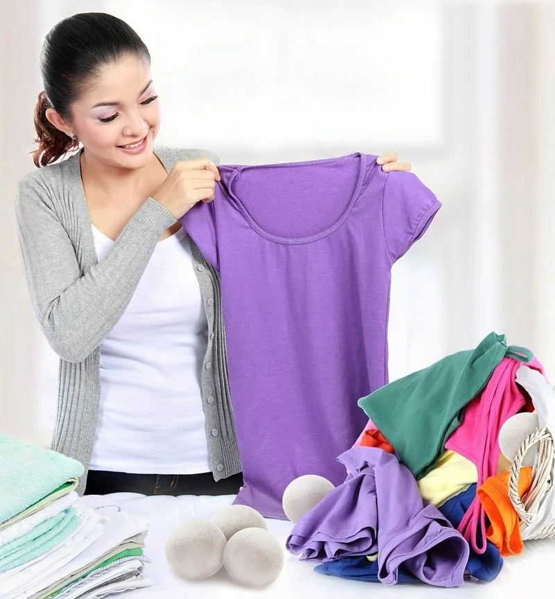 A woman holds up a purple t-shirt next to a pile of reusable wool dryer balls.