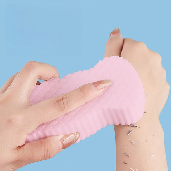 Hands hold a pink exfoliating bath sponge with fish scale texture against a light blue background.