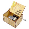 A small wooden music box with a lid featuring a sun design and intricate patterns, showing the hand-crank mechanism.