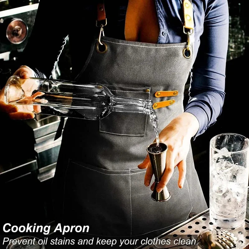 A person wearing a dark gray canvas cooking apron with tool pockets is pouring liquid from a glass bottle into a small metal 