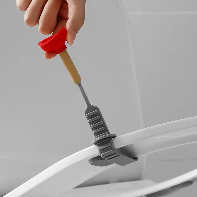 A hand is using a red and beige tool to lift the lid of a white portable toilet.