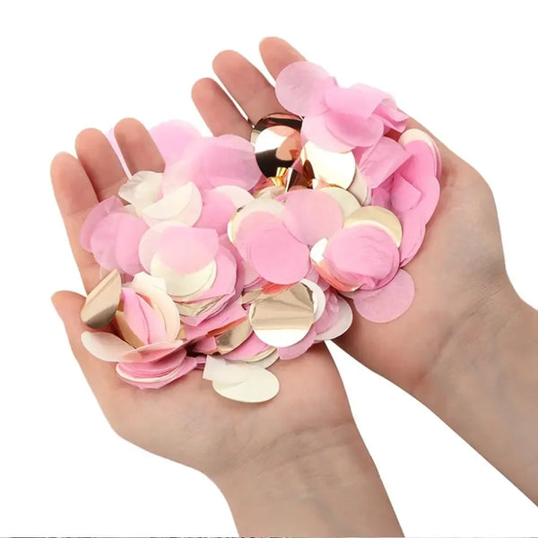 A hand holds a pile of pink and gold decorative confetti tissue paper for parties.