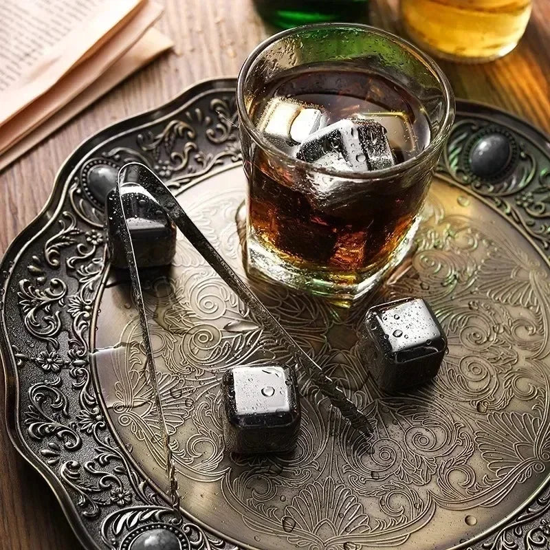 Reusable stainless steel whiskey ice cubes resting on an ornate metal tray with a glass of amber liquid.