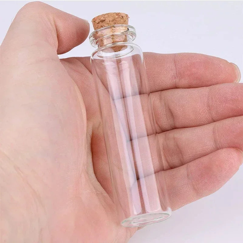 A hand holds a clear glass bottle with a cork stopper, used for DIY art and gifts.