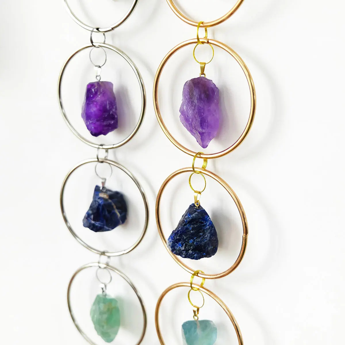 A collection of seven crystal healing ornaments featuring purple, blue, and green stones suspended on gold-toned rings.