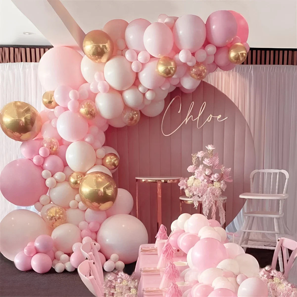 A pink and gold balloon garland decoration featuring round foil balloons and white balloons for an event backdrop.