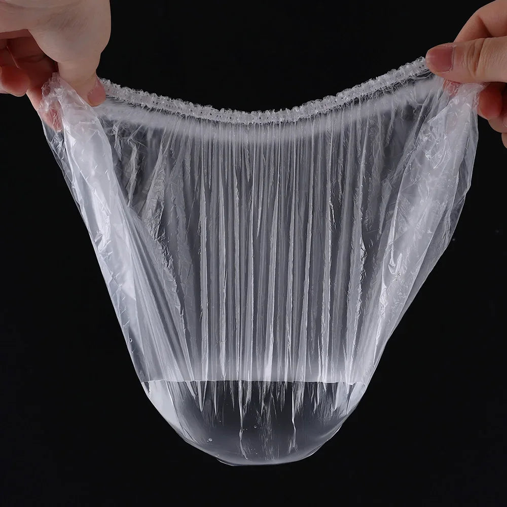 A hand is holding a clear, reusable disposable shower cap for hair protection, showing the mesh texture.