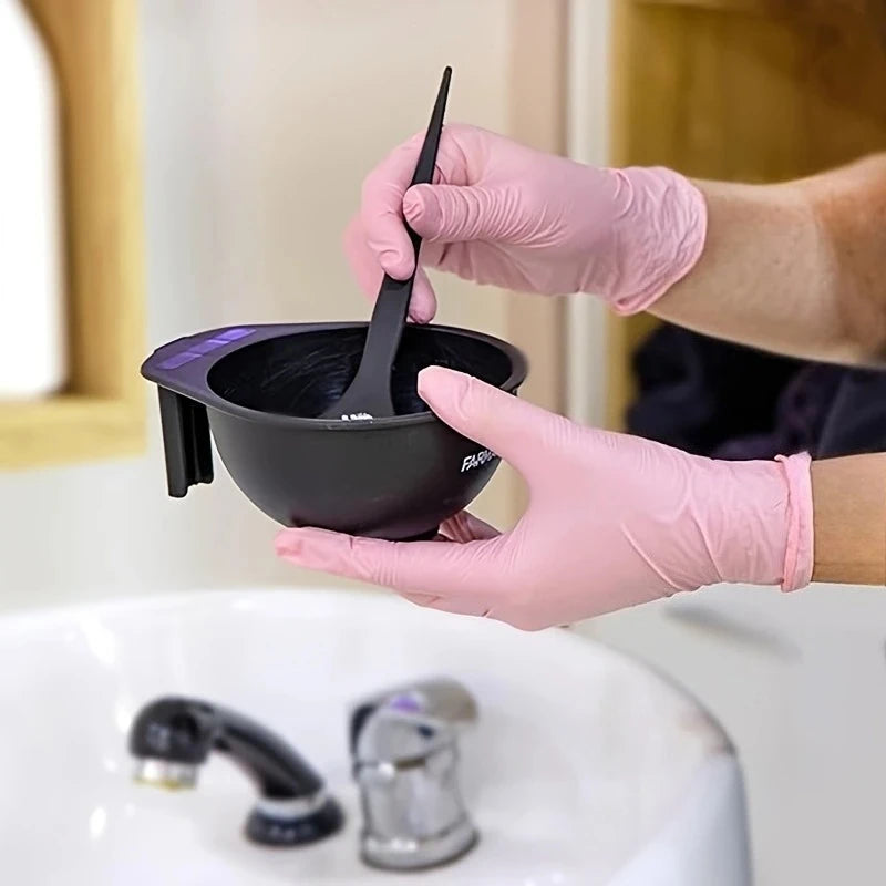 A hand wearing a pink nitrile glove is using a black silicone pot to clean a kitchen sink.