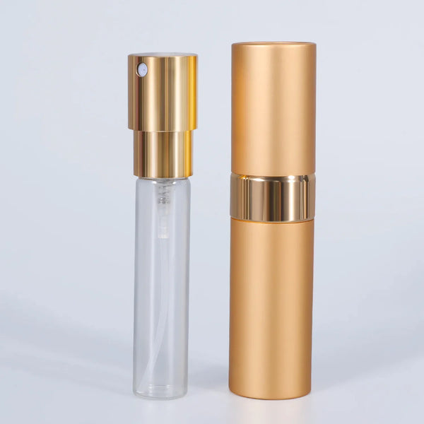 A tall, cylindrical perfume spray bottle with a clear glass body and gold-colored metal accents.