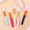 A collection of six silicone facial mask brushes in various colors including pink, orange, blue, and black, displayed on a li