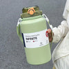 A light green stainless steel insulated tumbler with a lid and handle is held by a person.