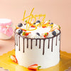 كعكة عيد ميلاد بيضاء مزينة بشرائح الفراولة والتوت الأزرق، تعلوها قطعة ذهبية مكتوب عليها عيد ميلاد سعيد.